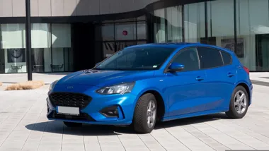 Niebieski hatchback zaparkowany przed nowoczesnym budynkiem.