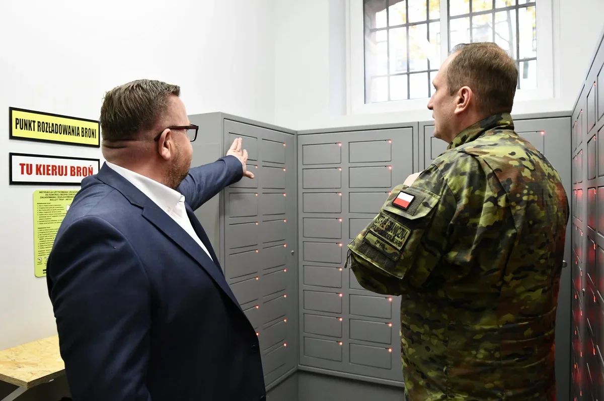 Dwaj mężczyźni, w tym żołnierz Wojsk Obrony Terytorialnej, stoją przy szafkach na broń w punkcie rozładowywania broni.
