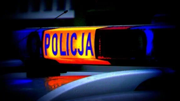 Migający sygnał świetlny z napisem POLICJA na dachu policyjnego pojazdu nocą.