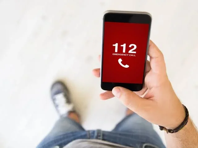 Mężczyzna trzyma w dłoni smartfon z czerwonym ekranem wyświetlającym numer alarmowy 112.