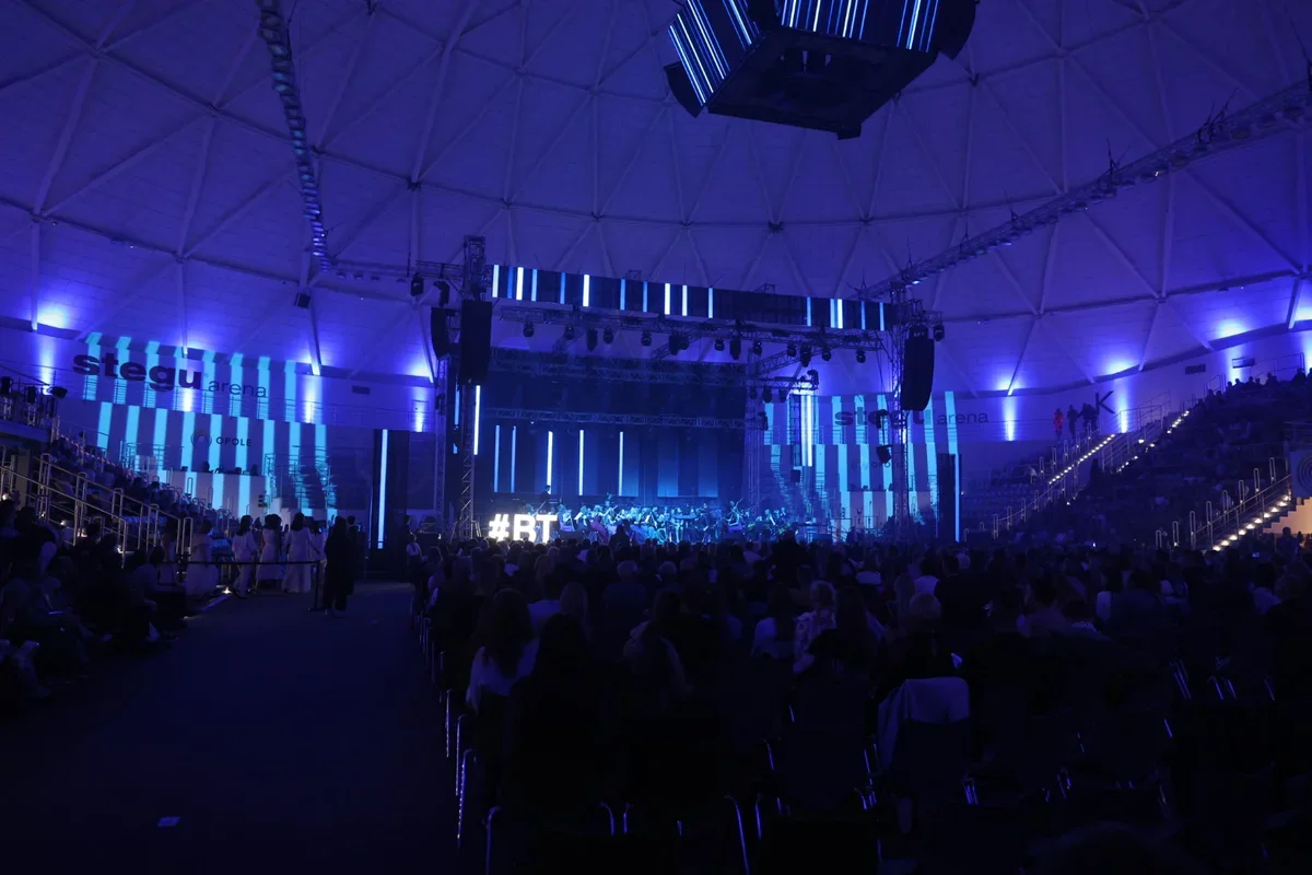 Widok na scenę i publiczność podczas wydarzenia w hali Stegu Arena oświetlonej na niebiesko.