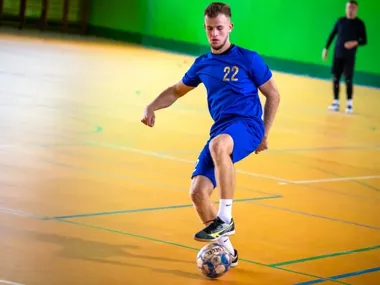 Mężczyzna w niebieskim stroju sportowym z numerem 22 gra w halową piłkę nożną na drewnianej boisku.