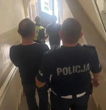 Funkcjonariusze policji prowadzą mężczyznę po schodach w budynku w kierunku wyjścia.