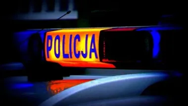 Migający sygnał świetlny z napisem POLICJA na dachu policyjnego pojazdu nocą.