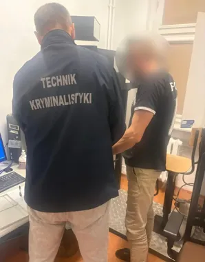 Technik kryminalistyki i policjant pracują przy urządzeniu w pomieszczeniu biurowym.