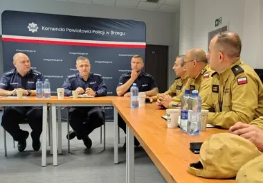 Funkcjonariusze policji i Straży Granicznej siedzą przy stołach podczas spotkania w sali Komendy Powiatowej Policji w Brzegu.