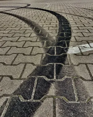 Fragment brukowanej nawierzchni z ciemnym, mokrym śladem w kształcie łuku oraz białą linią malowaną na kostce.