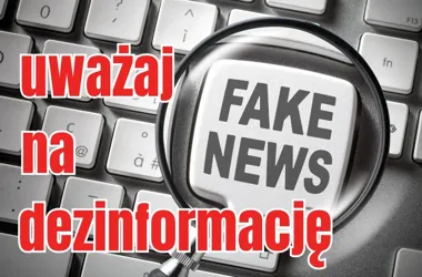 Fragment klawiatury komputerowej z powiększającym szkłem nad klawiszem z napisem „FAKE NEWS” oraz czerwonym hasłem „uważaj na dezinformację”.
