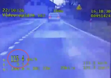 Zapis z policyjnej wideorejestratorowej kontroli prędkości pokazujący pojazd jadący drogą z wykazaną prędkością 115,4 km/h.