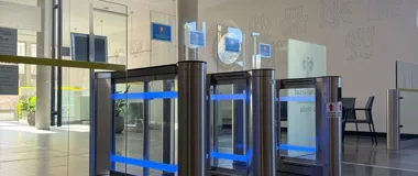 Nowoczesne bramki obrotowe z niebieskim podświetleniem w holu budynku użyteczności publicznej.